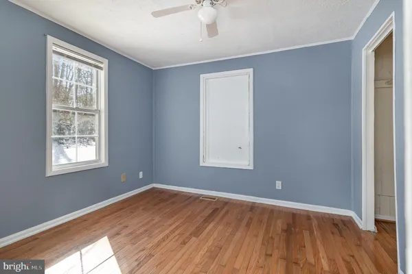 an empty room with wooden floor chandelier fan and windows