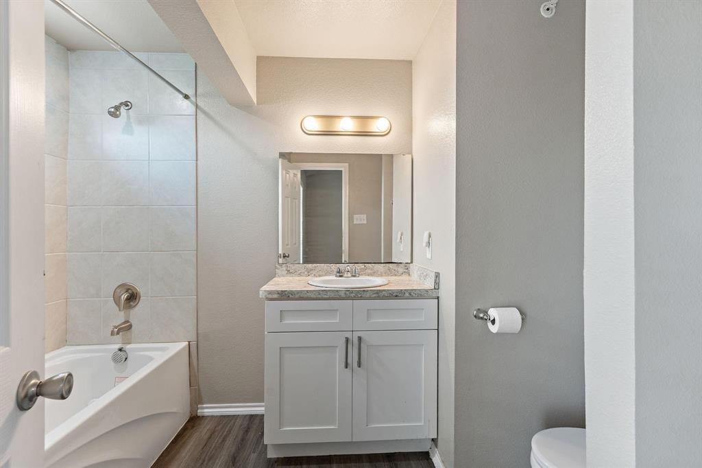 6108 Abrams Road, Unit 521 Dallas, TX 75231 - Photo 19 of 20 Full bathroom featuring a white bathtub with tile surround, a single vanity with a white countertop and basin sink, wood-finish flooring, and a wall-mounted light fixture