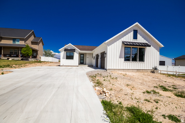 3322 250 S Street Vernal, UT 84078 - Photo 35 of 37 Contemporary farmhouse-style residence featuring white board and batten siding, dark trim windows, a prominent gable, a concrete driveway, and an attached two-car garage with wood-finish doors