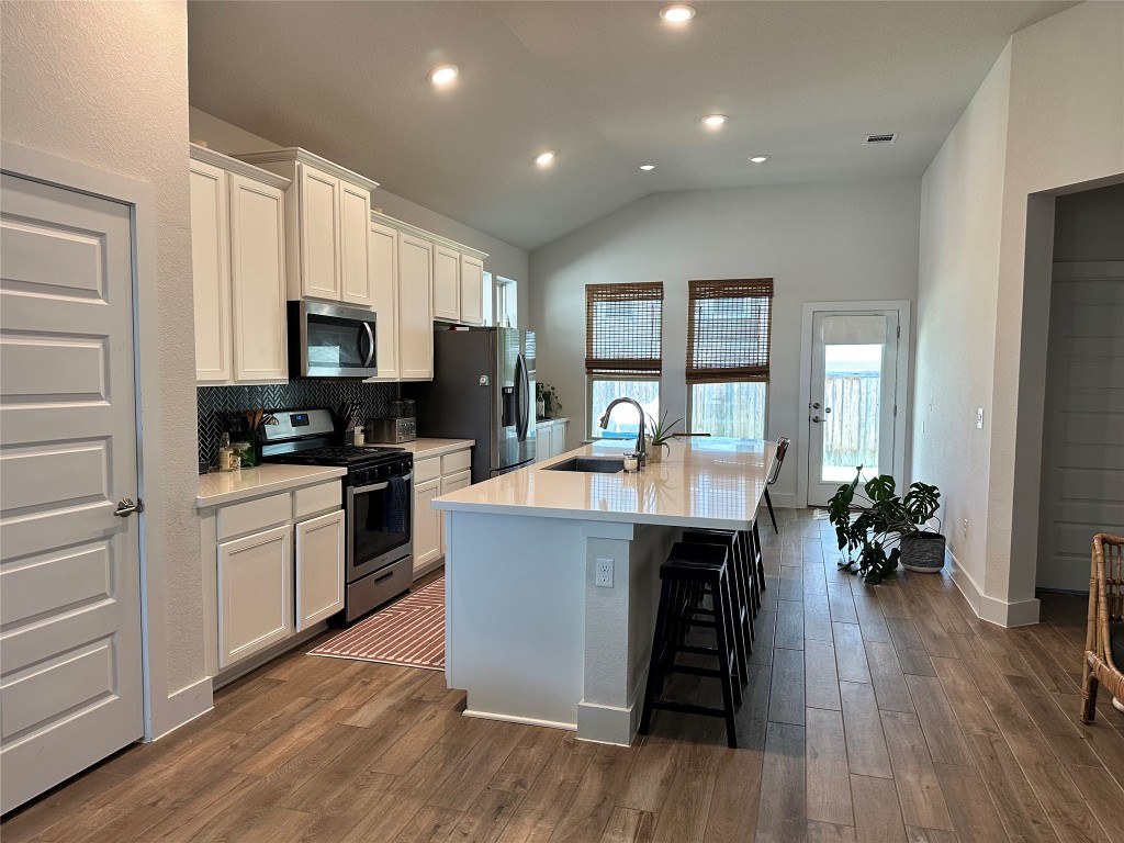 8600 Cumbrae Lane Austin, TX 78744 - Photo 4 of 29 Kitchen featuring decorative backsplash, appliances with stainless steel finishes, vaulted ceiling, a breakfast bar, and an island with sink