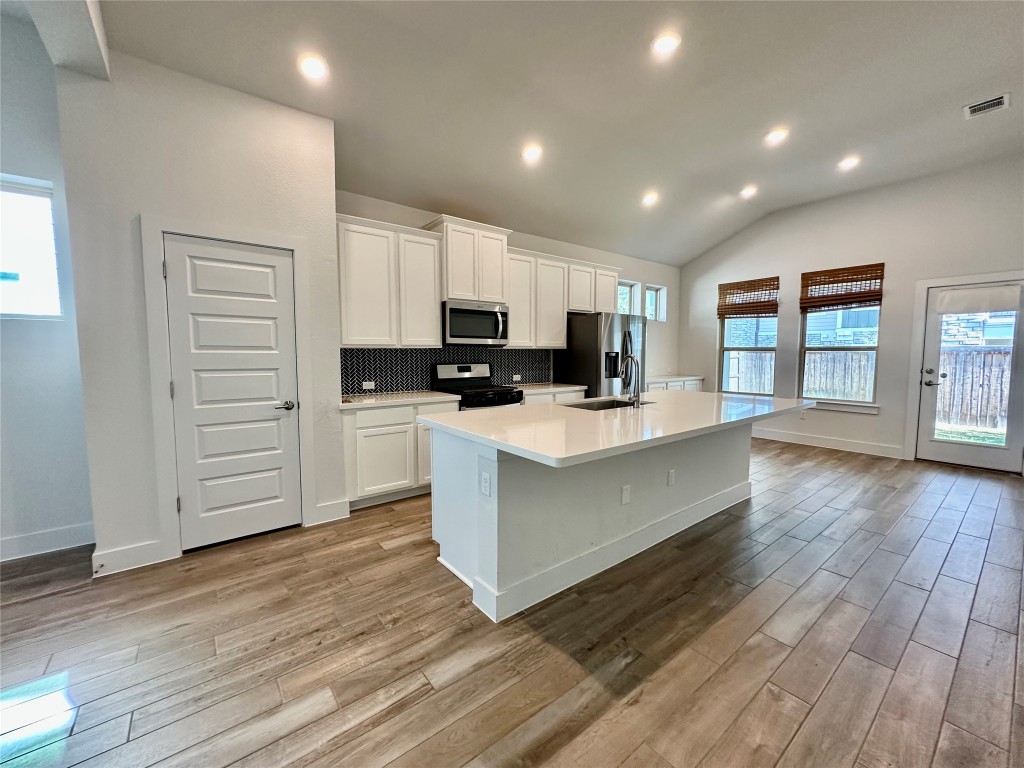 8600 Cumbrae Lane Austin, TX 78744 - Photo 6 of 29 Kitchen featuring decorative backsplash, lofted ceiling, white cabinets, a center island with sink, and recessed lighting