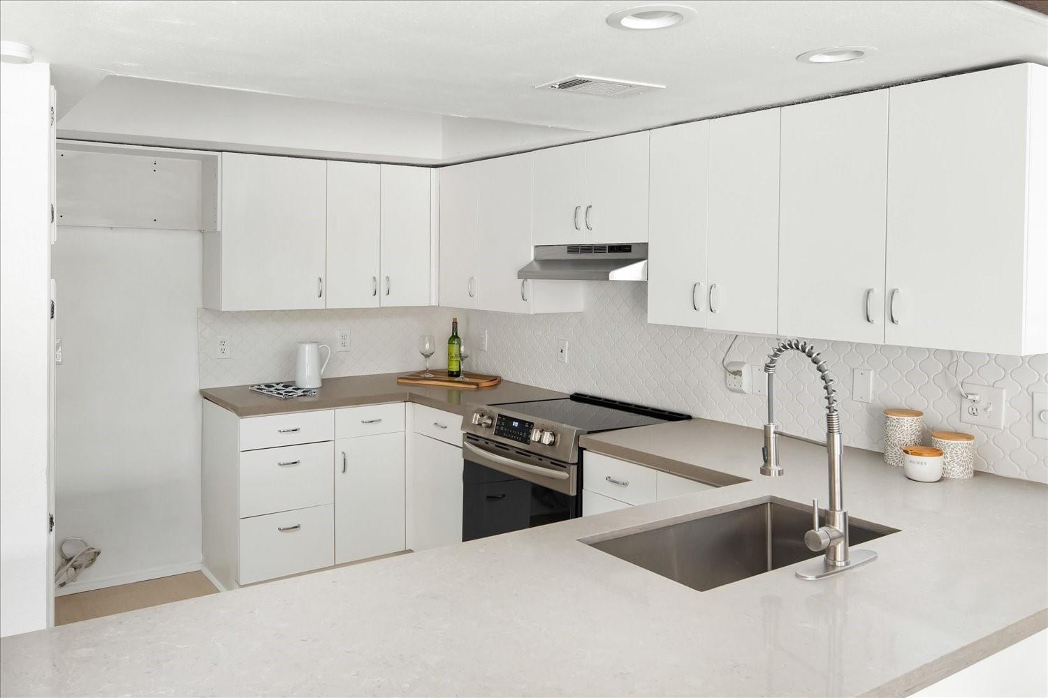 559 Demarett Drive Point Venture, TX 78645 - Photo 11 of 23 Kitchen with electric range, white cabinetry, under cabinet range hood, and backsplash