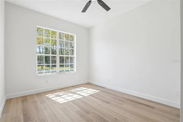 an empty room with wooden floor ceiling fan and windows
