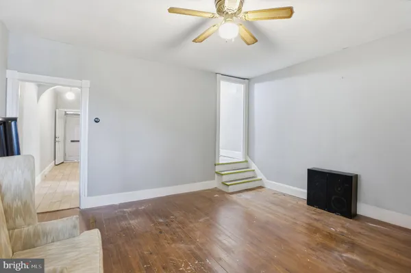 a view of an empty room with wooden floor and a ceiling fan