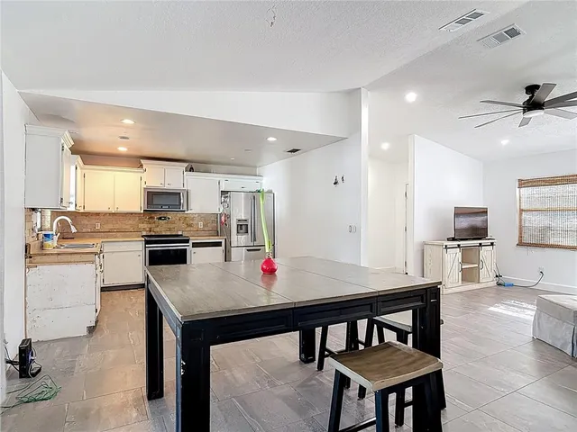 a kitchen with stainless steel appliances kitchen island granite countertop a dining table chairs refrigerator and sink