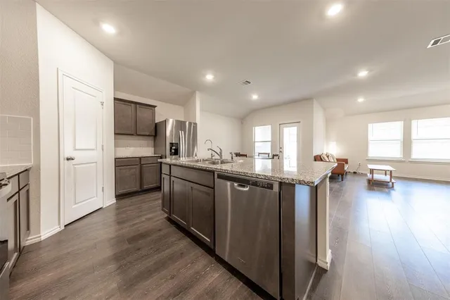 a kitchen with stainless steel appliances granite countertop a refrigerator a sink dishwasher a stove and white cabinets with wooden floor