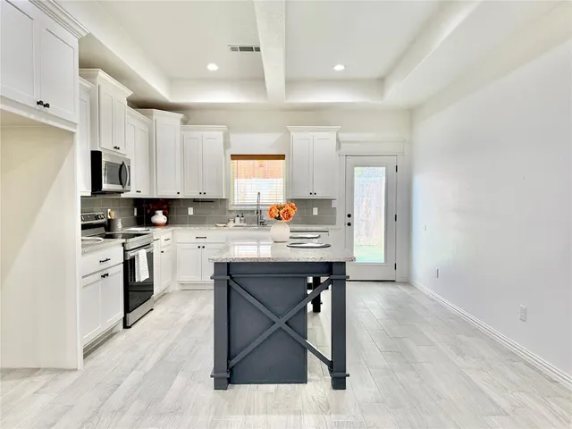 a kitchen with stainless steel appliances a stove a sink a refrigerator white cabinets and wooden floor