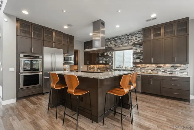 a kitchen with stainless steel appliances kitchen island granite countertop a kitchen island a stove a refrigerator a oven a sink with island and chairs
