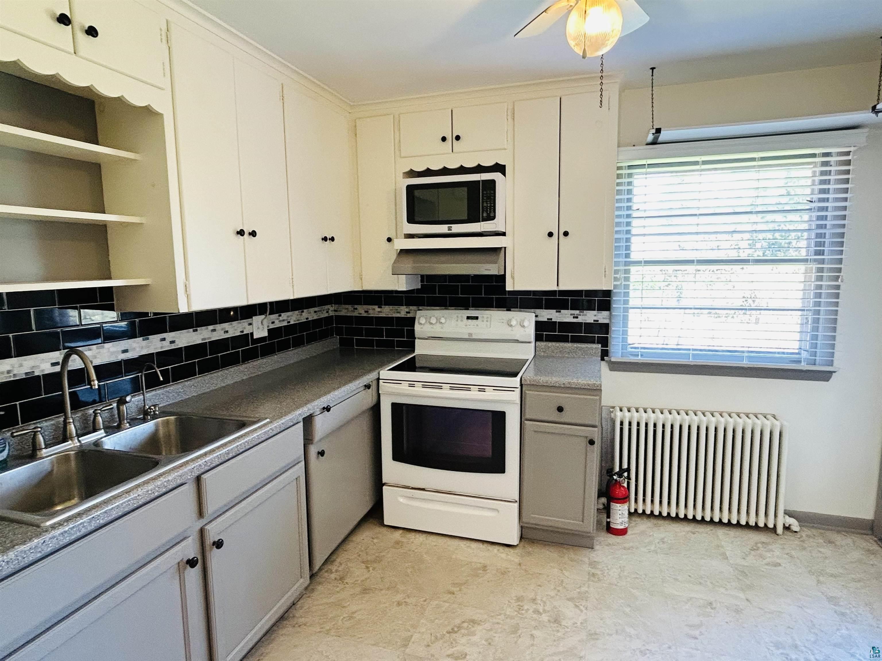 5090 London Road, Unit 1 Duluth, MN 55804 - Photo 7 of 54 Kitchen featuring white upper cabinetry, gray lower cabinetry, black subway tile backsplash with accent band, dual-basin stainless steel sink, and a white electric range with microwave above