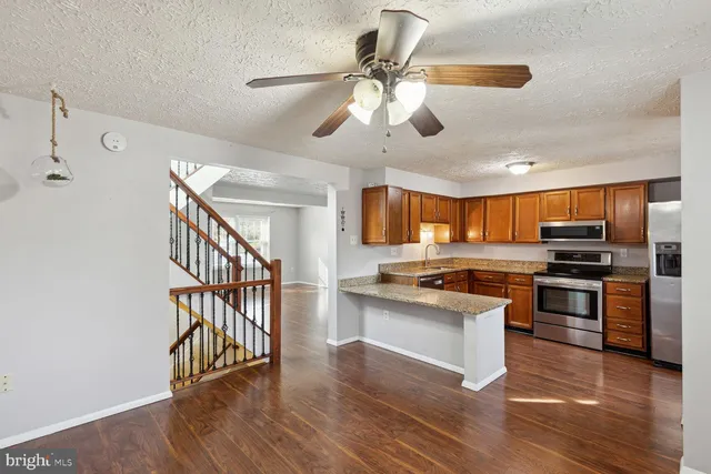 a kitchen with stainless steel appliances kitchen island granite countertop a stove top oven a sink a dining table and chairs with wooden floor