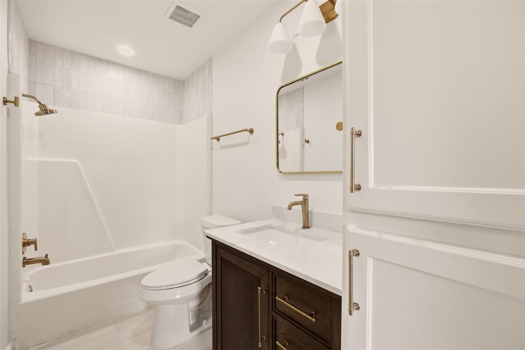 908 Isbell Road, Unit B Fort Worth, TX 76114 - Photo 23 of 27 Bathroom featuring a deep brown wood-finish vanity with a white countertop and gold-tone hardware, a rectangular framed mirror, a shower-tub combination with white subway tile surround, and gold-tone fixtures