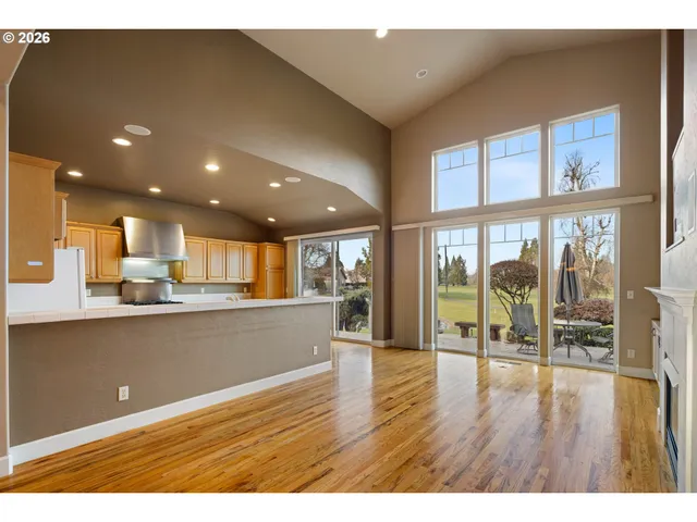 a living room with stainless steel appliances wooden floor dining table and a large window