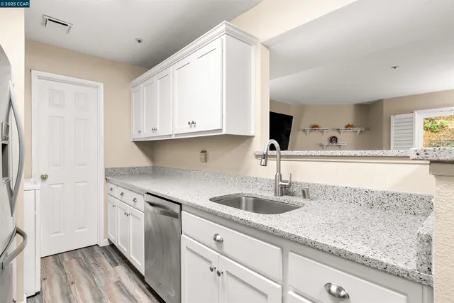a kitchen with stainless steel appliances granite countertop a sink and white cabinets with wooden floor