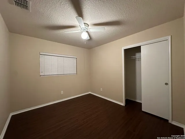 a view of an empty room with wooden floor and a ceiling fan