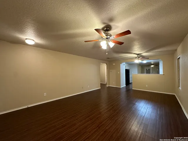 an empty room with wooden floor chandelier fan and windows