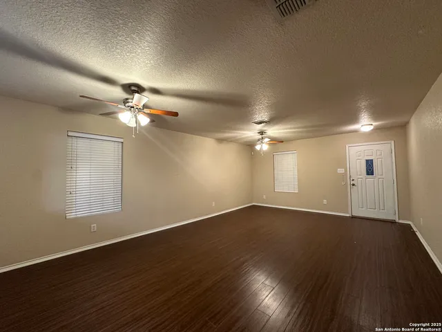 a view of an empty room with wooden floor and fan