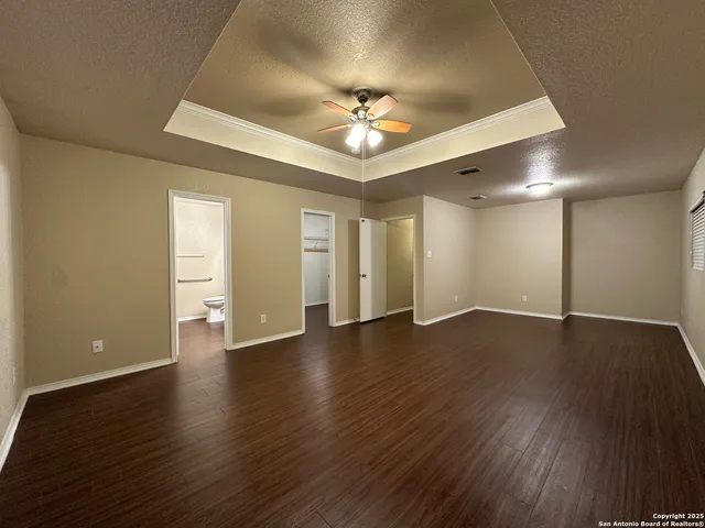 a view of an empty room with wooden floor and a ceiling fan