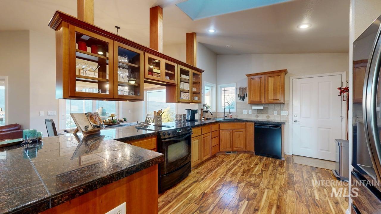 1724 Ridgeview Drive Clarkston, WA 99403 - Photo 5 of 48 Kitchen featuring glass insert cabinets, brown cabinetry, black appliances, vaulted ceiling, and backsplash