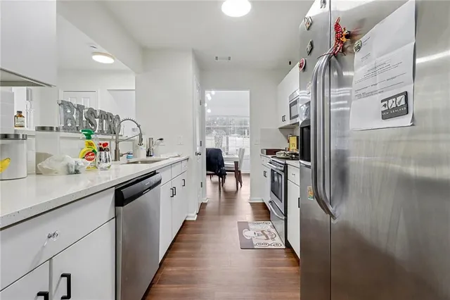 a kitchen with stainless steel appliances a stove top oven a sink a refrigerator white cabinets and wooden floor