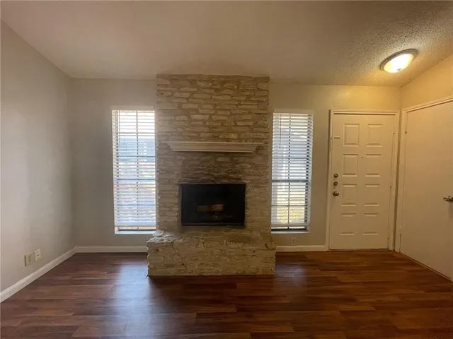an empty room with wooden floor fireplace and windows
