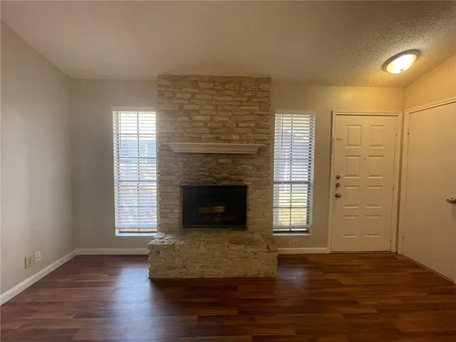 an empty room with wooden floor fireplace and windows