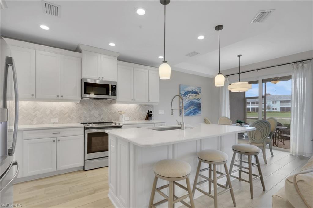 2647 Seychelles Circle, Unit 2202 Naples, FL 34112 - Photo 7 of 37 Kitchen with stainless steel appliances, light wood-type flooring, an island with sink, a kitchen breakfast bar, and white cabinets