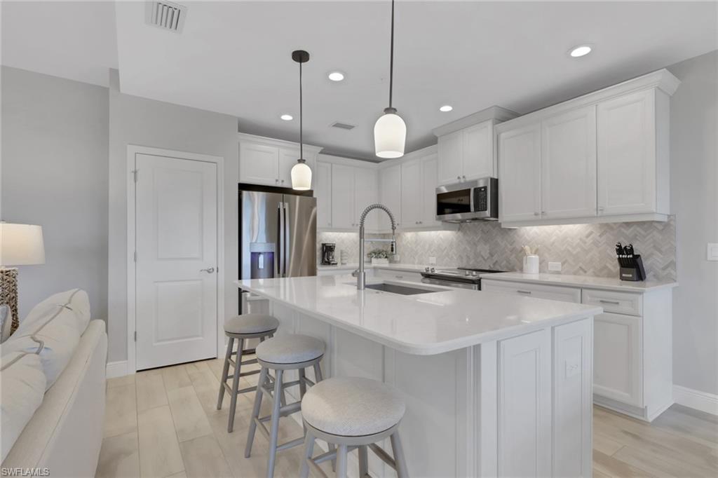 2647 Seychelles Circle, Unit 2202 Naples, FL 34112 - Photo 8 of 37 Kitchen with white cabinets, a kitchen breakfast bar, a center island with sink, stainless steel appliances, and light stone counters