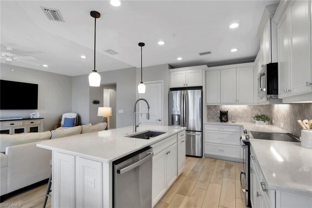 2647 Seychelles Circle, Unit 2202 Naples, FL 34112 - Photo 37 of 37 Kitchen featuring open floor plan, a breakfast bar, stainless steel appliances, wood tiled floors, and white cabinets