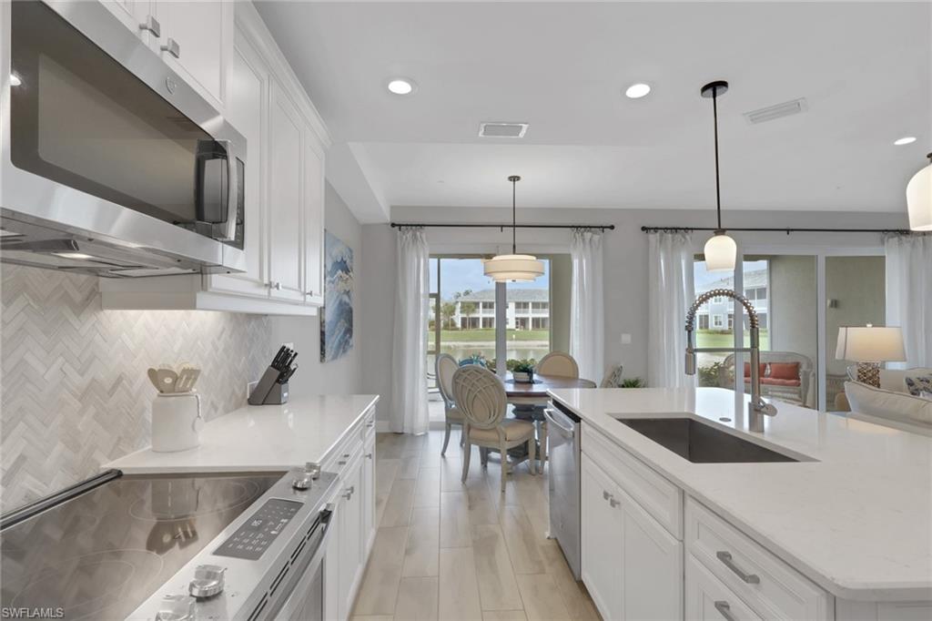 2647 Seychelles Circle, Unit 2202 Naples, FL 34112 - Photo 9 of 37 Kitchen featuring white cabinets, stainless steel appliances, light stone countertops, hanging light fixtures, and a center island with sink