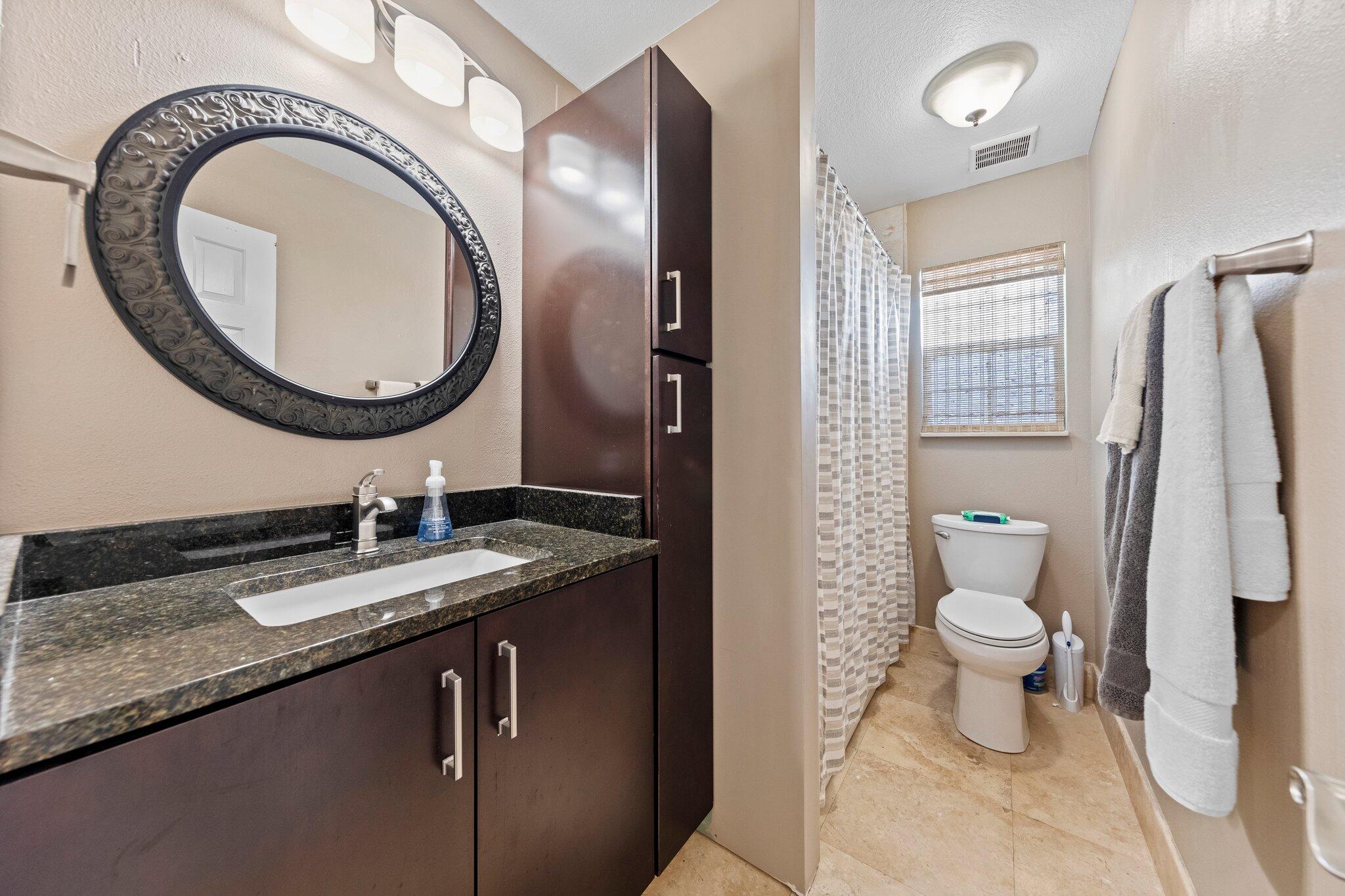 704 Main Street Destin, FL 32541 - Photo 29 of 59 a bathroom with a granite countertop toilet a sink and a mirror