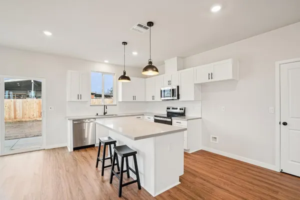a kitchen with stainless steel appliances a stove a sink dishwasher a refrigerator white cabinets and wooden floor next to a window