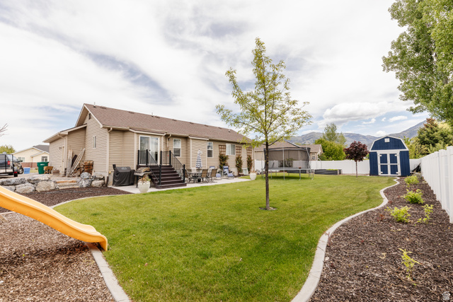 972 West 2840th Street South Logan, UT 84321 - Photo 36 of 46 Expansive backyard featuring a lush lawn, a multi-level deck with black railings, a dedicated patio area, a contrasting blue storage shed, and a white privacy fence