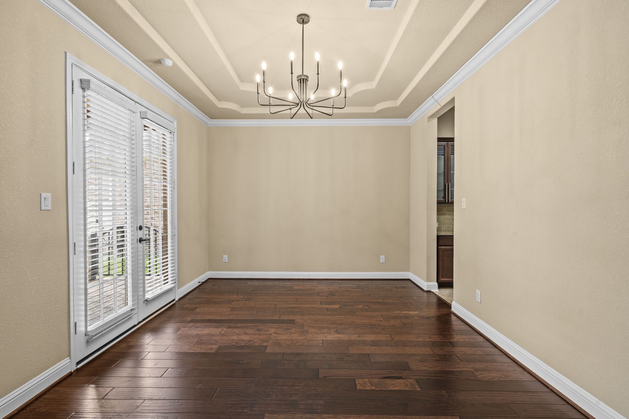 14215 Spindle Arbor Road Cypress, TX 77429 - Photo 17 of 47 This room features elegant hardwood floors, a stylish chandelier, and French doors with blinds leading to the outdoors. The tray ceiling adds a touch of sophistication, and the neutral walls provide a versatile backdrop.