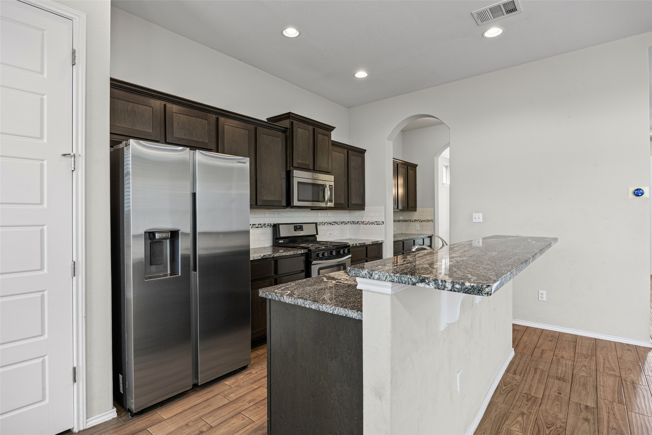 17401 Silent Harbor Loop Pflugerville, TX 78660 - Photo 14 of 37 Kitchen featuring stainless steel appliances, arched walkways, dark wood finish cabinets, dark stone counters, and tasteful backsplash