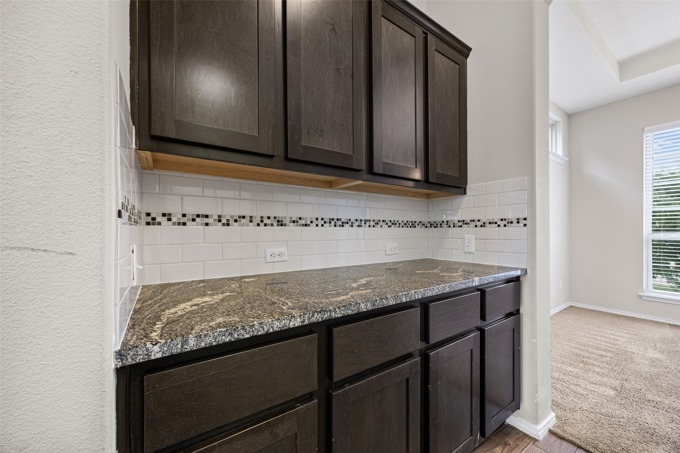 17401 Silent Harbor Loop Pflugerville, TX 78660 - Photo 9 of 37 Kitchen featuring dark wood finish cabinets, dark stone counters, backsplash, and light wood-type flooring