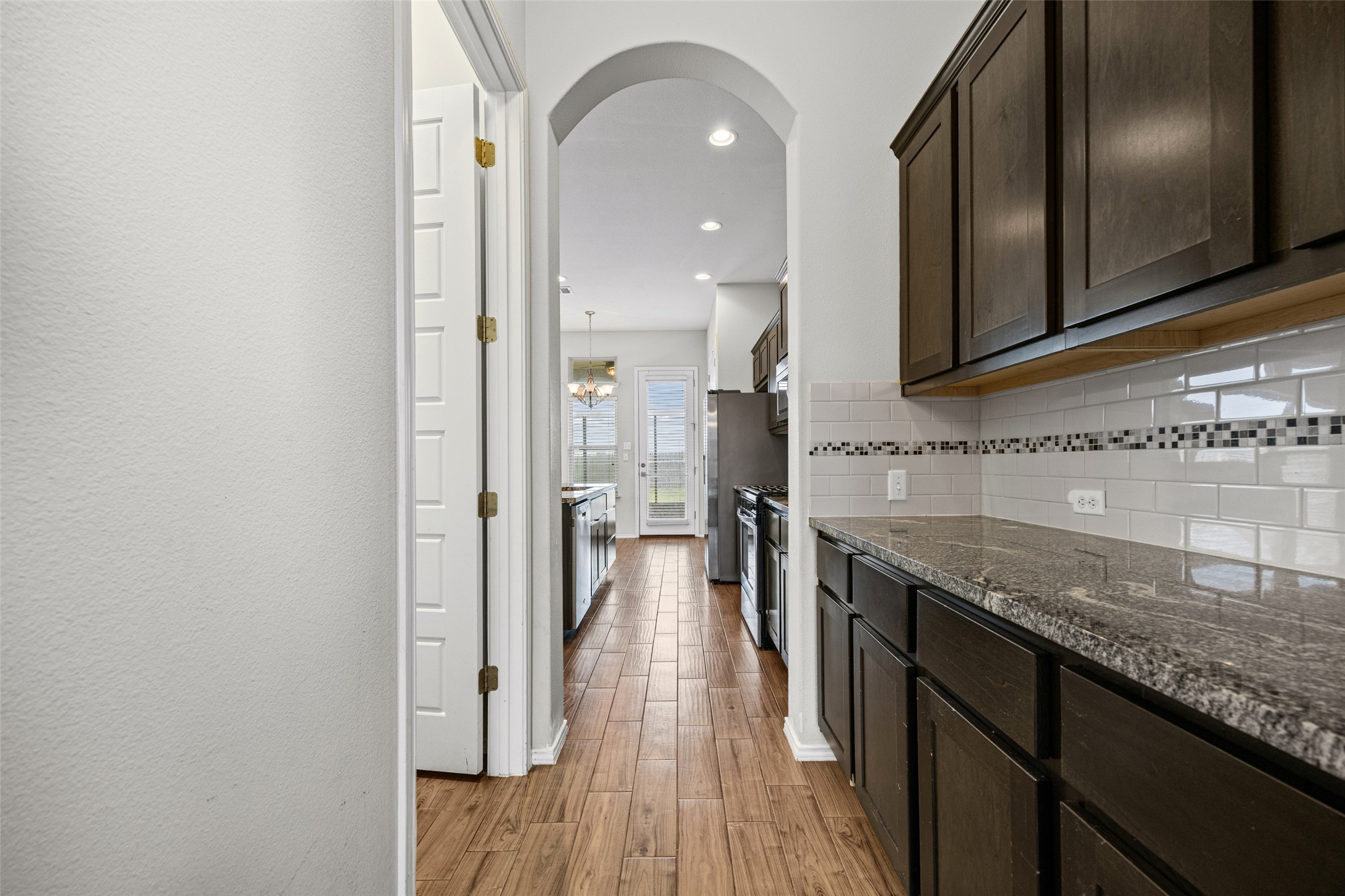 17401 Silent Harbor Loop Pflugerville, TX 78660 - Photo 10 of 37 Kitchen featuring dark wood finish cabinetry, arched walkways, light wood finished floors, dark stone counters, and recessed lighting