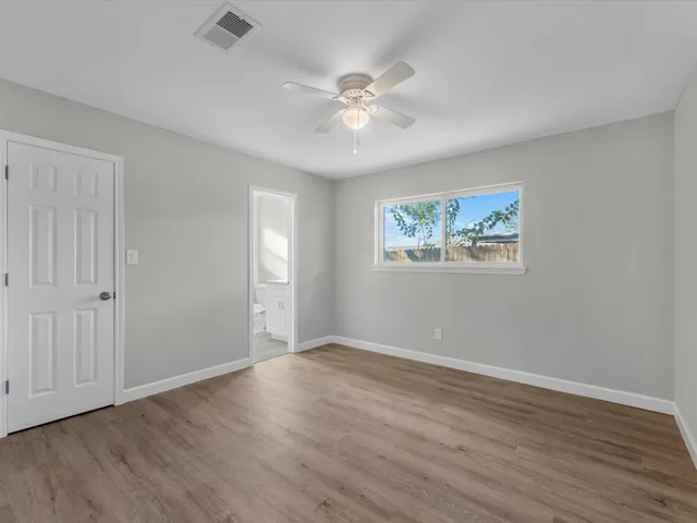 a view of an empty room with wooden floor and a ceiling fan