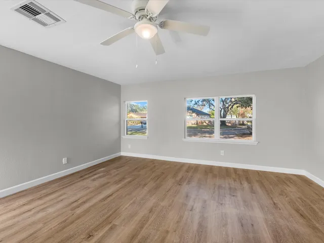 an empty room with wooden floor chandelier fan and windows