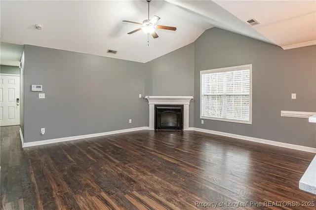 a view of an empty room with wooden floor fireplace and a window