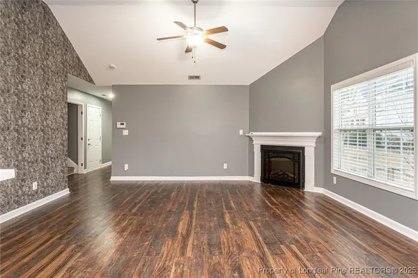 a view of an empty room with wooden floor fireplace and a window