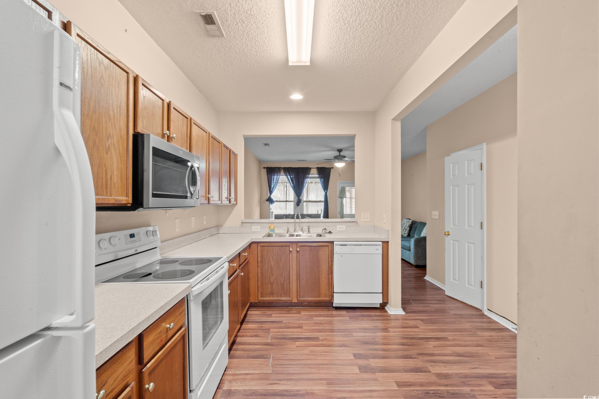 322 Kiskadee Loop, Unit 12E Conway, SC 29526 - Photo 4 of 36 Kitchen featuring white appliances, light wood-style flooring, a textured ceiling, brown cabinets, and ceiling fan