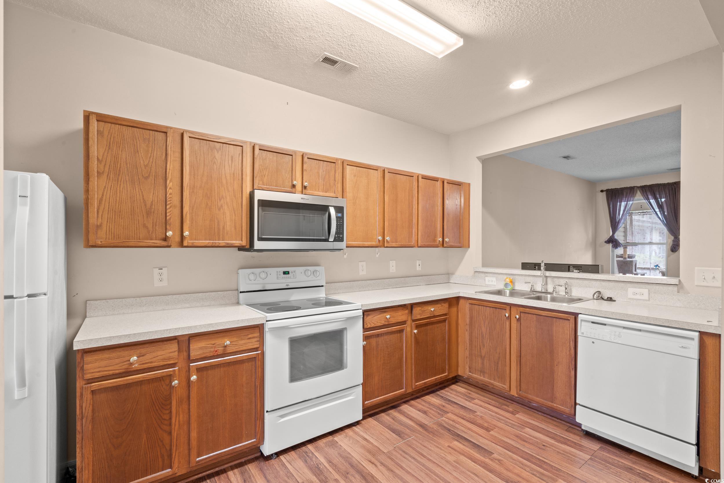 322 Kiskadee Loop, Unit 12E Conway, SC 29526 - Photo 5 of 36 Kitchen with white appliances, light countertops, a textured ceiling, light wood-type flooring, and brown cabinets