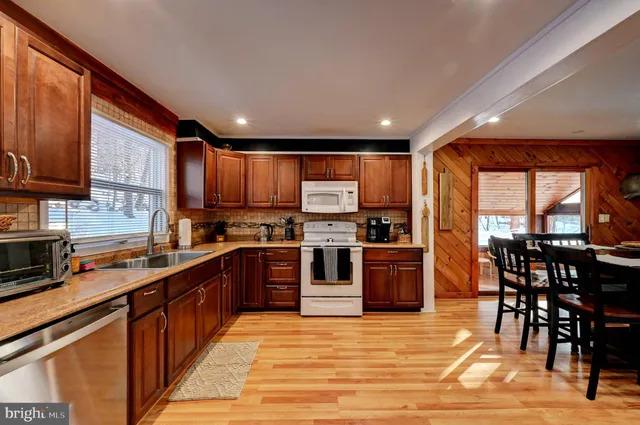 a kitchen with stainless steel appliances granite countertop a stove top oven a sink dishwasher a dining table and chairs with wooden floor