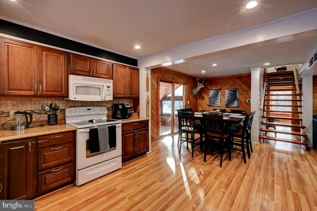 a kitchen with stainless steel appliances granite countertop a stove top oven a refrigerator a dining table and chairs with wooden floor