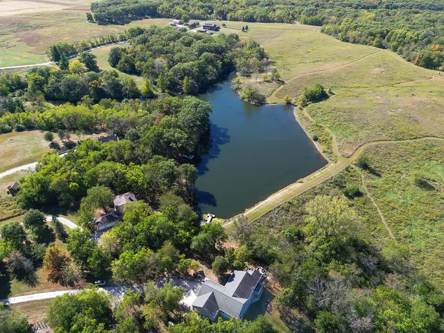 a view of a lake with lawn chairs and large trees