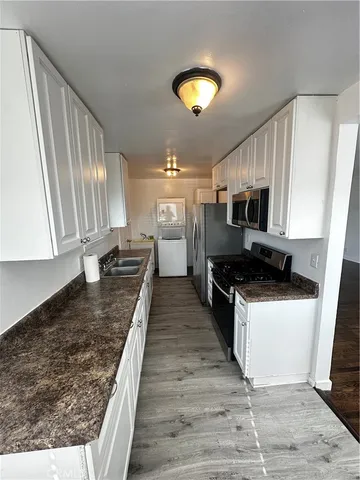 a large kitchen with stainless steel appliances granite countertop a stove a sink dishwasher and a microwave oven with white cabinets