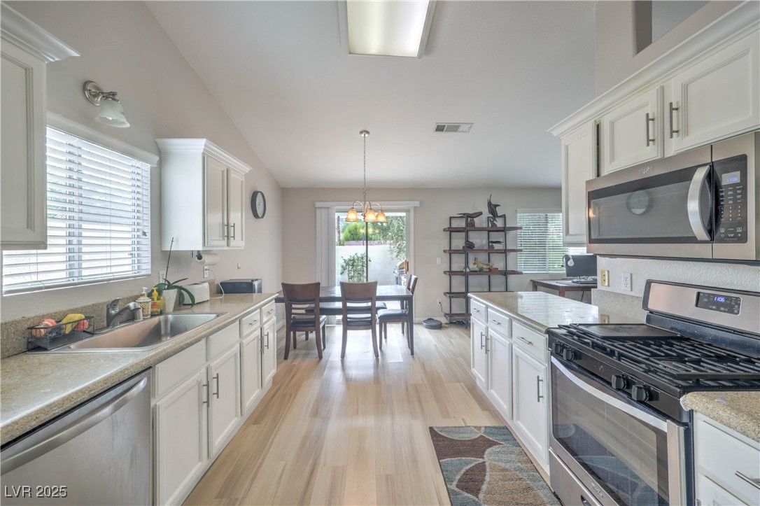 47 Trailside Court Henderson, NV 89012 - Photo 8 of 26 Kitchen featuring appliances with stainless steel finishes, light wood-style floors, decorative light fixtures, white cabinetry, and a chandelier