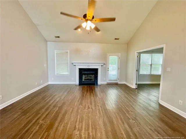 an empty room with wooden floor fireplace and windows