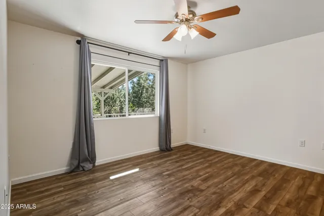 an empty room with wooden floor fan and windows