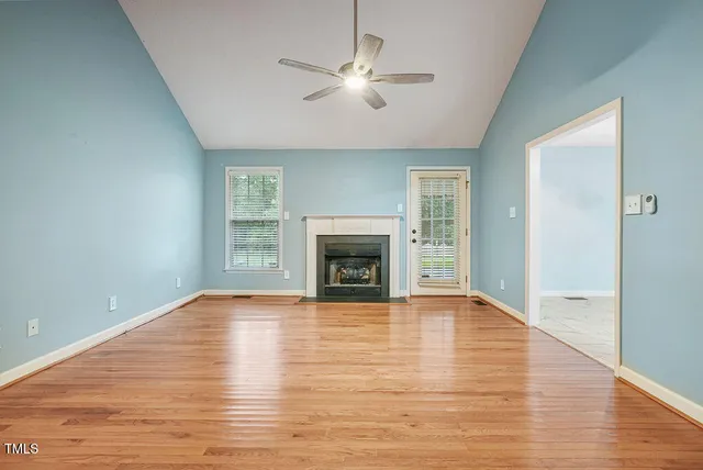 a view of an empty room with wooden floor fireplace and a window